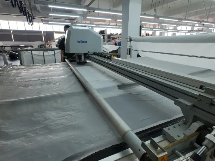 Industrial textile manufacturing machine in a factory setting with workers overseeing the process.
