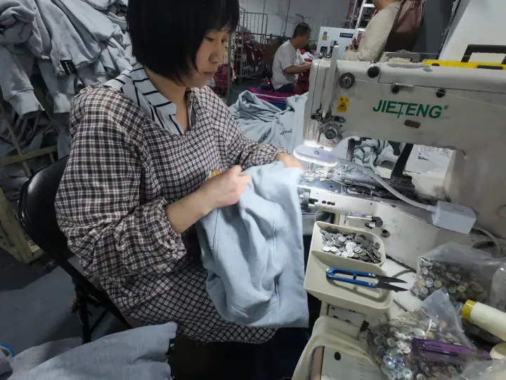 Woman sewing fabric on industrial sewing machine in a clothing factory, focusing on quality control and production efficiency.