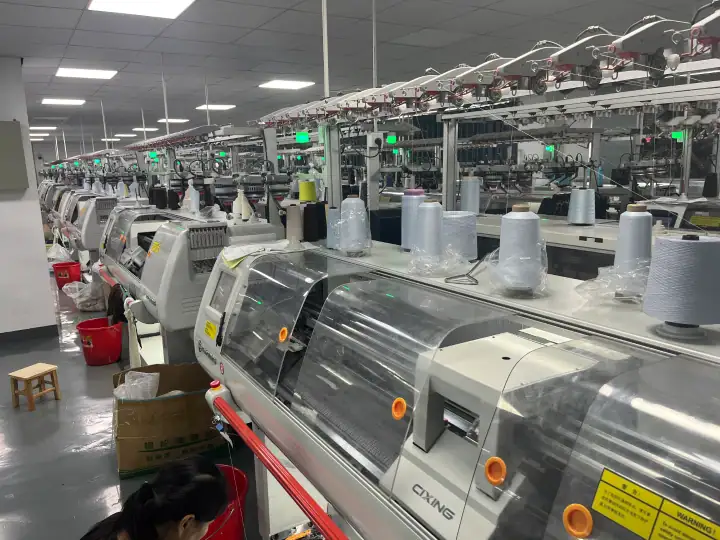 Interior view of a textile manufacturing factory with automated sewing machines and spools of thread, showcasing modern industrial textile production.
