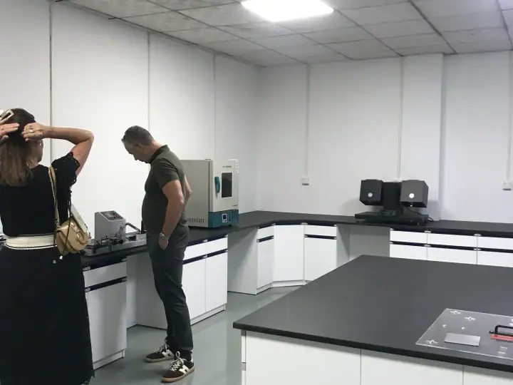 Two people in a clean, modern laboratory with white cabinets and black countertops, engaging with scientific instruments and devices.