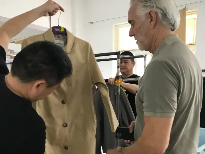 Senior man and young designer examining a beige blazer in a fashion workshop setting.