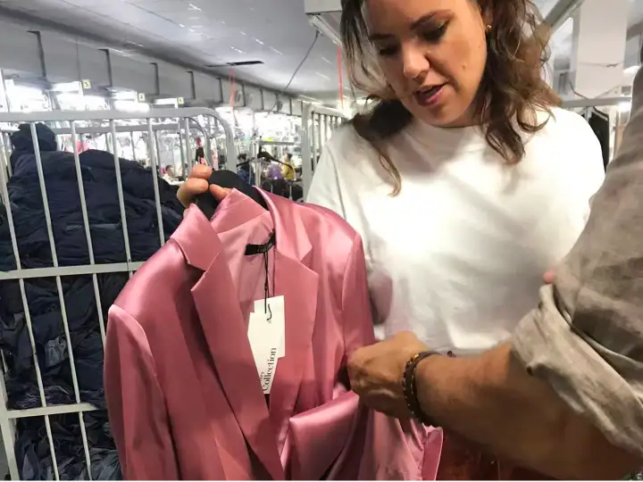 Woman shopping for a pink blazer at a clothing store, with racks of clothes in the background.