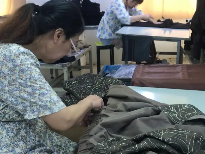 Women working on fabric sewing and embroidery in a classroom setting, focusing on textile craftsmanship.