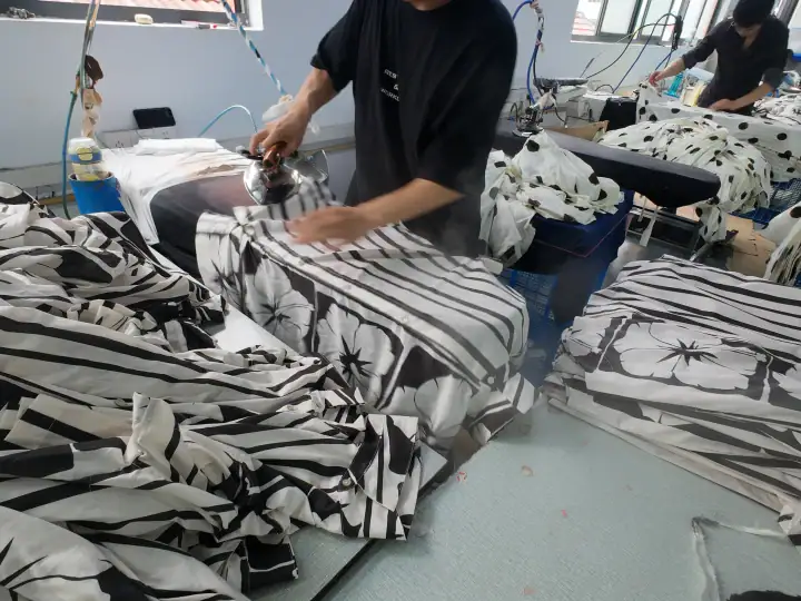 Workers at NBFish Fashion are printing black and white floral fabric patterns using heat transfer techniques in a modern factory setting.