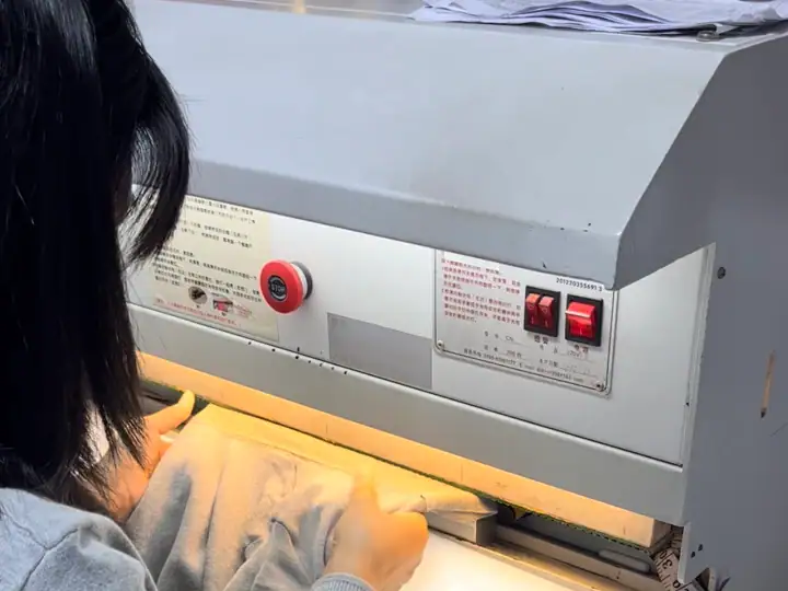 Close-up of a person operating an industrial fabric cutting machine with safety controls and illuminated workspace.
