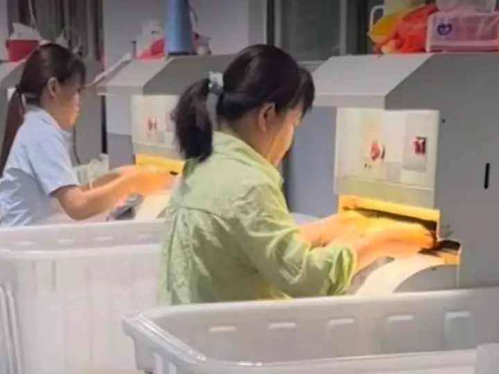 Two female workers operating jewelry manufacturing machines in a factory setting, wearing protective gloves and focused on their tasks.