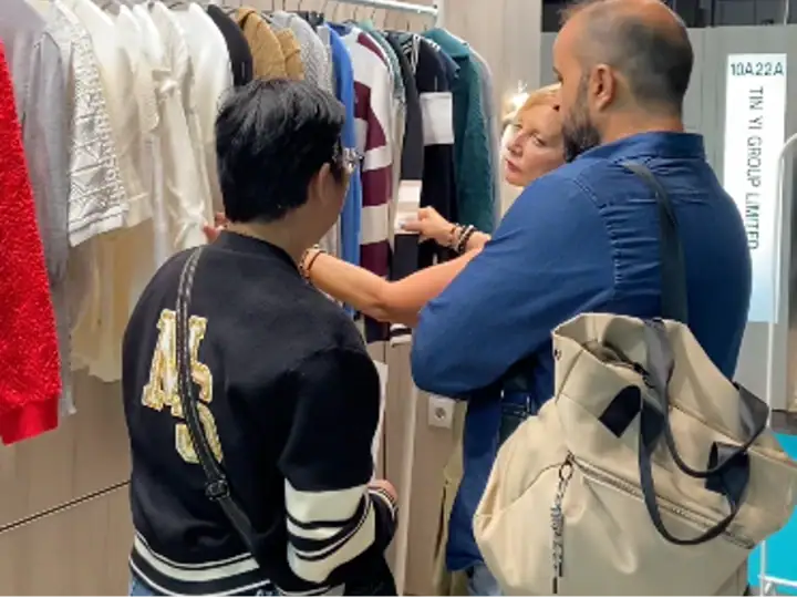 Group of three people shopping for clothing in a retail store, discussing and examining garments on racks.