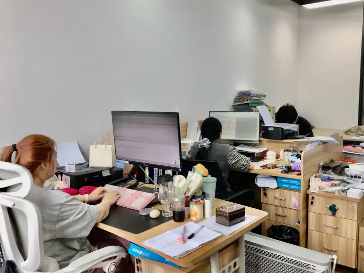 Office workspace with employees working at desks, computers, and office supplies in a modern, organized environment.