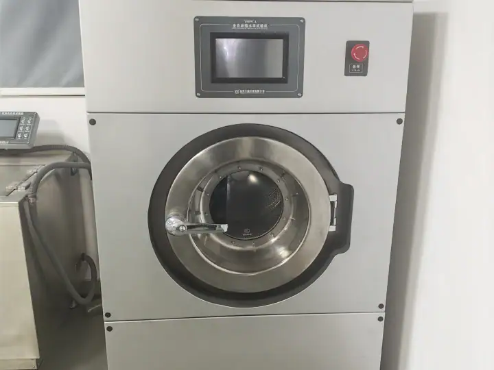 Large industrial washing machine with digital control panel and stainless steel drum in a laundry facility.
