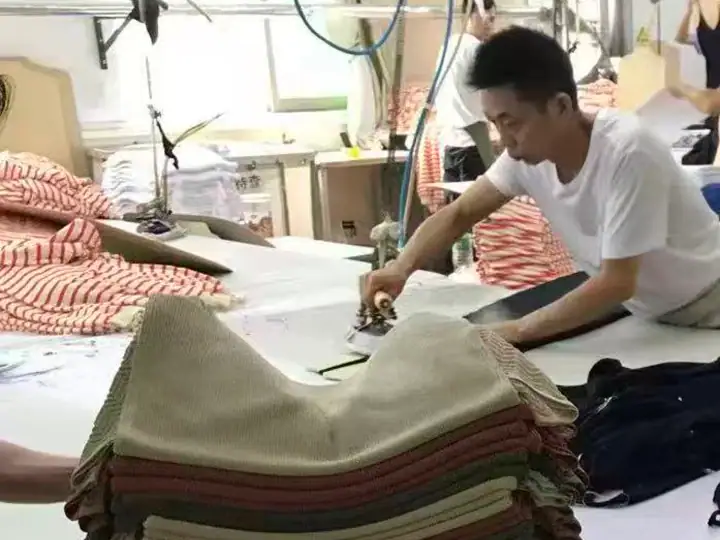 Young man working on fabric samples in a fashion design studio with sewing tools and fabric stacks.
