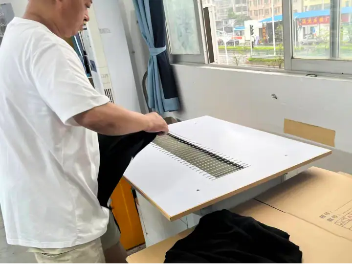 Worker inspecting fabric on a production table in a textile factory with large windows and natural light.