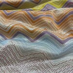 Close-up of vibrant zigzag patterned fabric with multicolored threads, showcasing intricate weaving details and a textured surface.