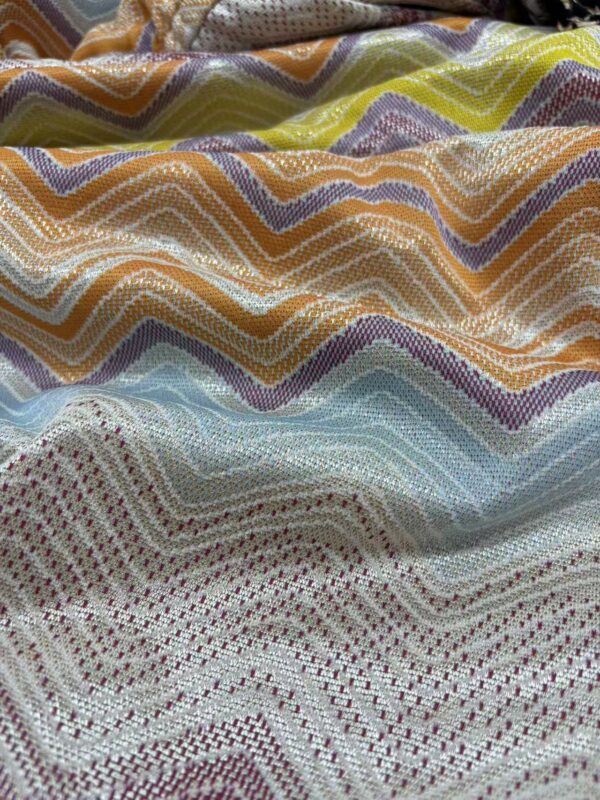 Close-up of vibrant zigzag patterned fabric with multicolored threads, showcasing intricate weaving details and a textured surface.