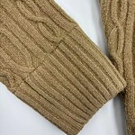 Close-up of a beige cable-knit sweater sleeve showing intricate knitting pattern and texture.