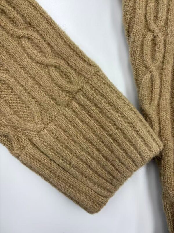 Close-up of a beige cable-knit sweater sleeve showing intricate knitting pattern and texture.