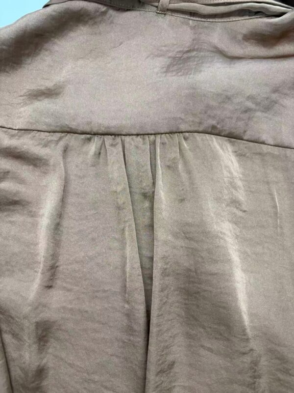 Close-up of beige dress fabric with pleats and stitching, showcasing high-quality material and craftsmanship.