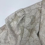 Close-up of a beige linen blouse with puffed sleeves and subtle print, perfect for casual or formal wear.