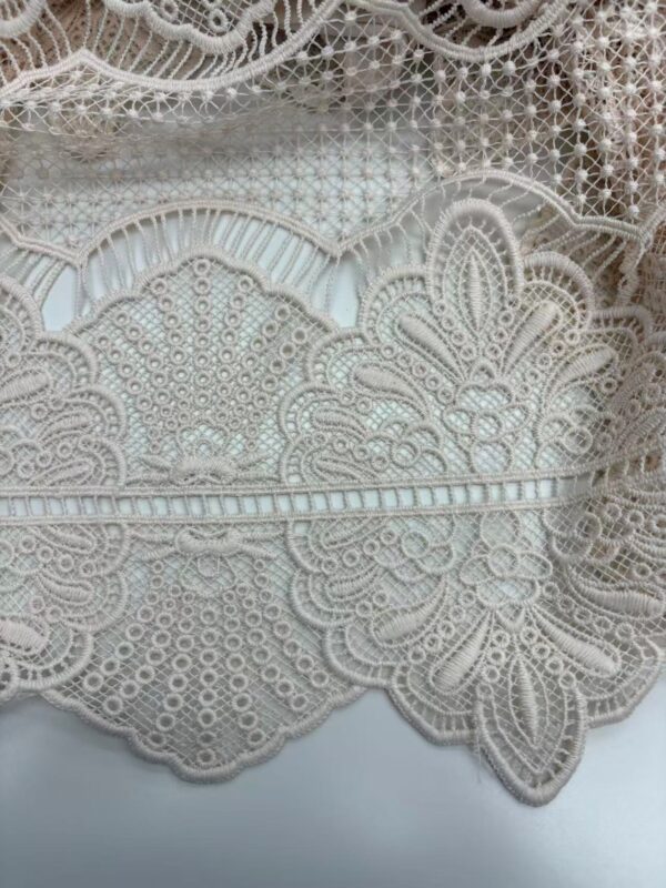Close-up of intricate white lace fabric with floral and geometric patterns, ideal for fashion and wedding dress embellishments.