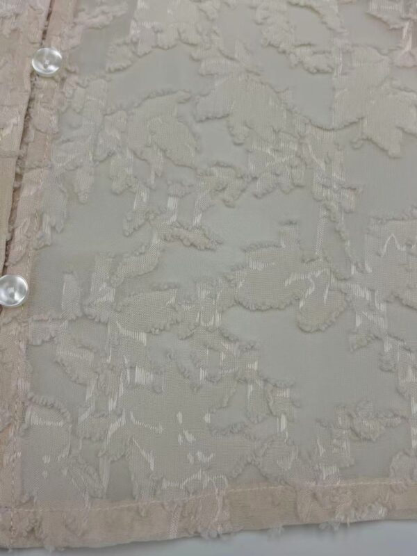 Close-up of delicate beige lace fabric with intricate floral patterns and pearl button details, ideal for wedding dresses and evening wear.