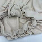 Close-up of a cream-colored zip-up hoodie with a front pocket and drawstrings, made from soft fabric, laid flat on a white surface.