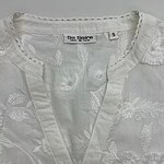 Close-up of a white embroidered blouse with floral patterns and a small button at the neckline, perfect for stylish summer wear.