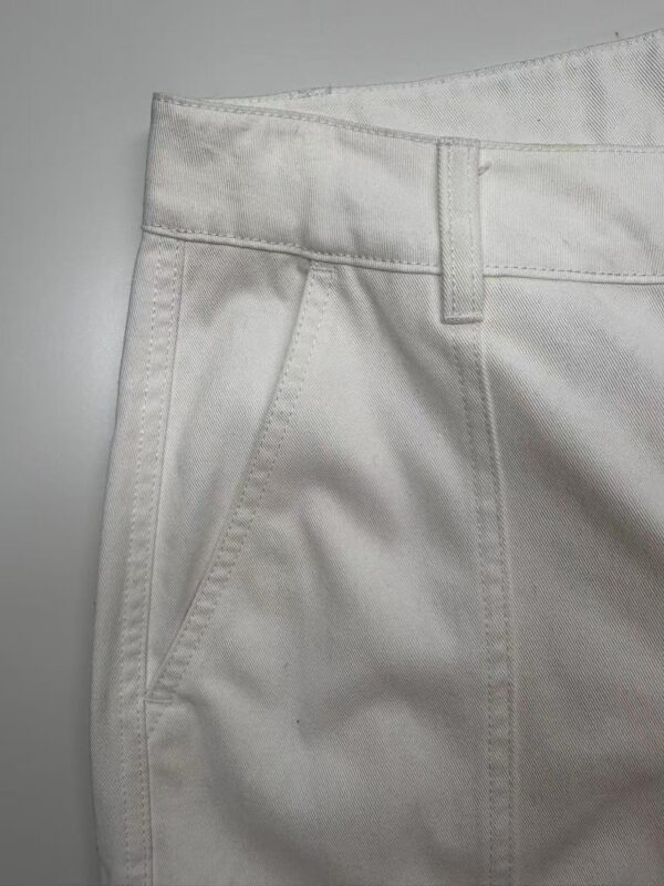 Close-up of white casual pants showing fabric texture, waistband, and front pocket design, ideal for fashion and clothing SEO.