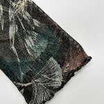 Close-up of a fabric with a detailed floral pattern in dark green, black, and beige tones, showcasing fine textile craftsmanship.