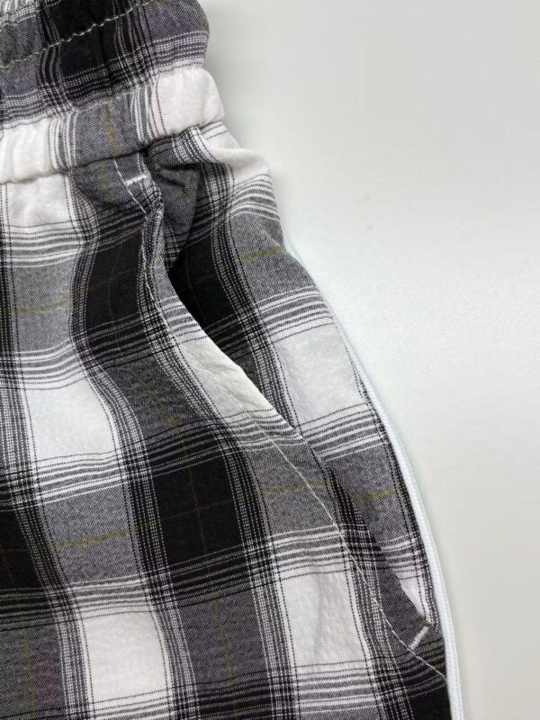 Close-up of plaid fabric with black, white, and gray pattern and a white zipper on the side.