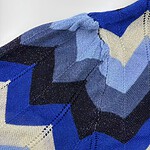 Close-up of a vibrant, geometric knitted textile with shades of blue, black, and beige, showcasing intricate patterns and craftsmanship.