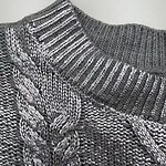 Close-up of a gray cable knit sweater with ribbed collar, showcasing detailed knitting pattern and texture.