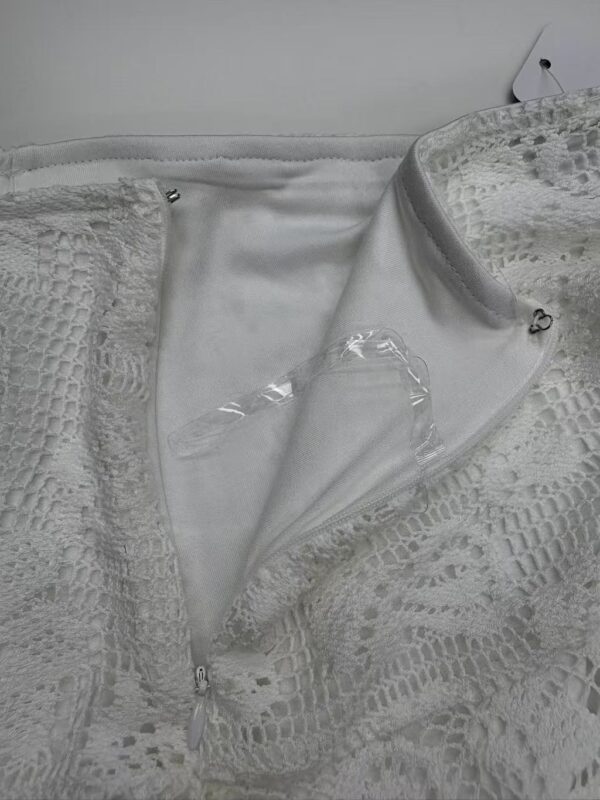 Close-up of a white lace dress with a zipper, showcasing intricate lace patterns and delicate fabric details for stylish women's fashion.