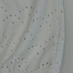 Close-up of white eyelet fabric with embroidered eyelet holes and delicate embroidery, showcasing fine craftsmanship and lightweight material.