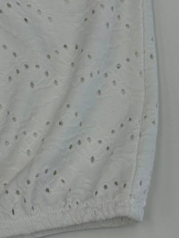 Close-up of white eyelet fabric with embroidered eyelet holes and delicate embroidery, showcasing fine craftsmanship and lightweight material.