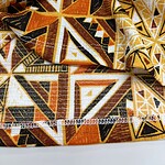 Close-up of vibrant African tribal pattern fabric with geometric shapes in orange, black, white, and yellow, suitable for fashion and textile design.