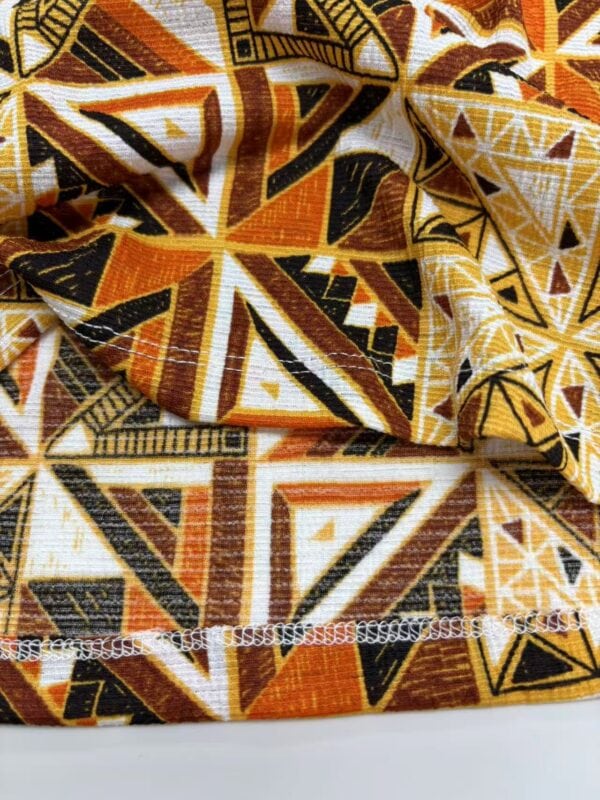 Close-up of vibrant African tribal pattern fabric with geometric shapes in orange, black, white, and yellow, suitable for fashion and textile design.