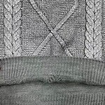 Close-up of a gray knit sweater featuring a cable pattern and ribbed hem, showcasing detailed knitting craftsmanship and cozy fabric.