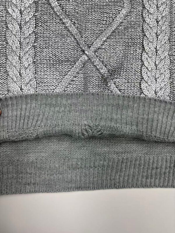 Close-up of a gray knit sweater featuring a cable pattern and ribbed hem, showcasing detailed knitting craftsmanship and cozy fabric.