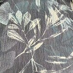 Close-up of fabric with botanical print featuring leaves and branches in muted tones, ideal for fashion and home decor.