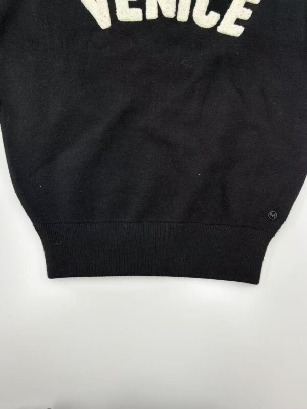 Close-up of a black sweatshirt featuring the word 'Venice' in white letters, showcasing casual fashion style.