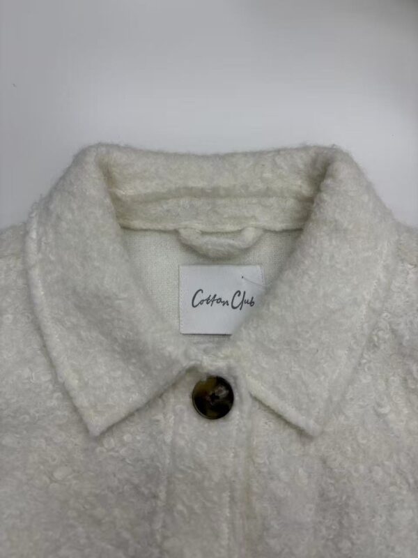 Close-up of a white cotton coat with a textured fabric and a single button, perfect for stylish winter wear.