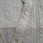 Close-up of delicate lace fabric with pearl buttons, showcasing intricate floral patterns and fine craftsmanship.