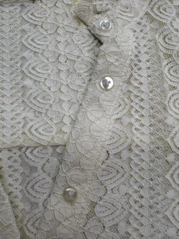 Close-up of delicate lace fabric with pearl buttons, showcasing intricate floral patterns and fine craftsmanship.