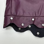Close-up of a stylish fashion bag featuring a purple faux leather surface, metal studs, and a scalloped black trim for a trendy look.