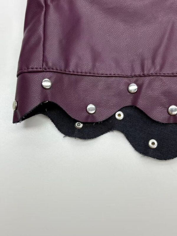 Close-up of a stylish fashion bag featuring a purple faux leather surface, metal studs, and a scalloped black trim for a trendy look.
