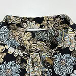 Close-up of a women's shirt with a floral pattern in shades of blue, beige, and black, featuring a button closure and detailed fabric design.