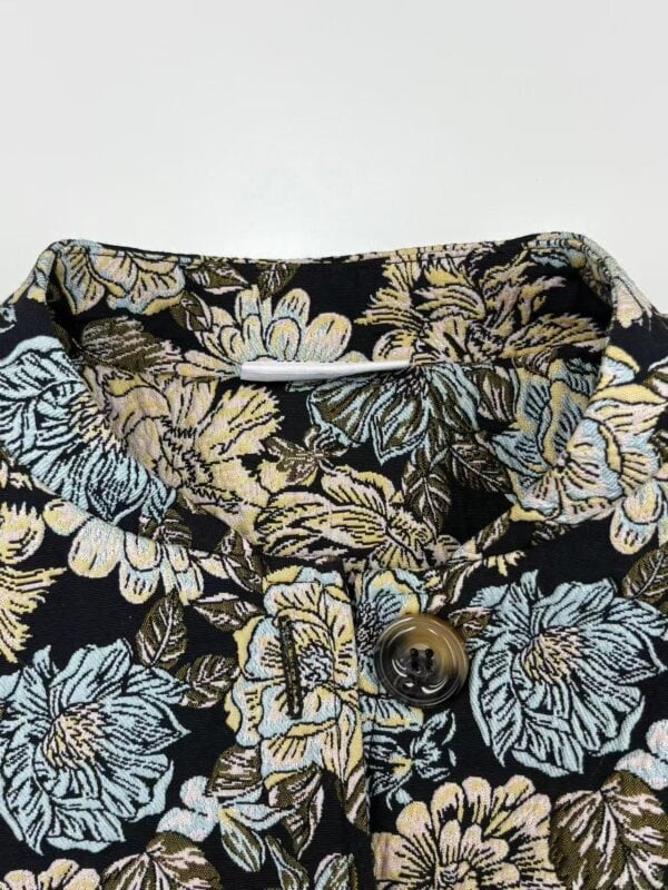 Close-up of a women's shirt with a floral pattern in shades of blue, beige, and black, featuring a button closure and detailed fabric design.