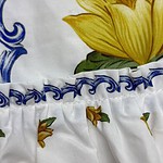 Close-up of a fabric with a vibrant yellow flower, blue decorative elements, and small yellow flowers with green leaves on a white background.