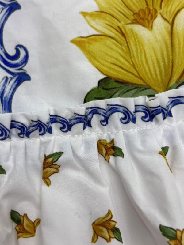 Close-up of a fabric with a vibrant yellow flower, blue decorative elements, and small yellow flowers with green leaves on a white background.
