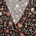Close-up of a women's dress with a black background and intricate floral print in shades of pink, red, and beige, featuring a V-neckline.