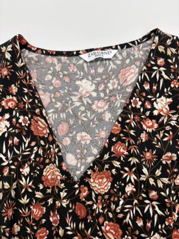 Close-up of a women's dress with a black background and intricate floral print in shades of pink, red, and beige, featuring a V-neckline.